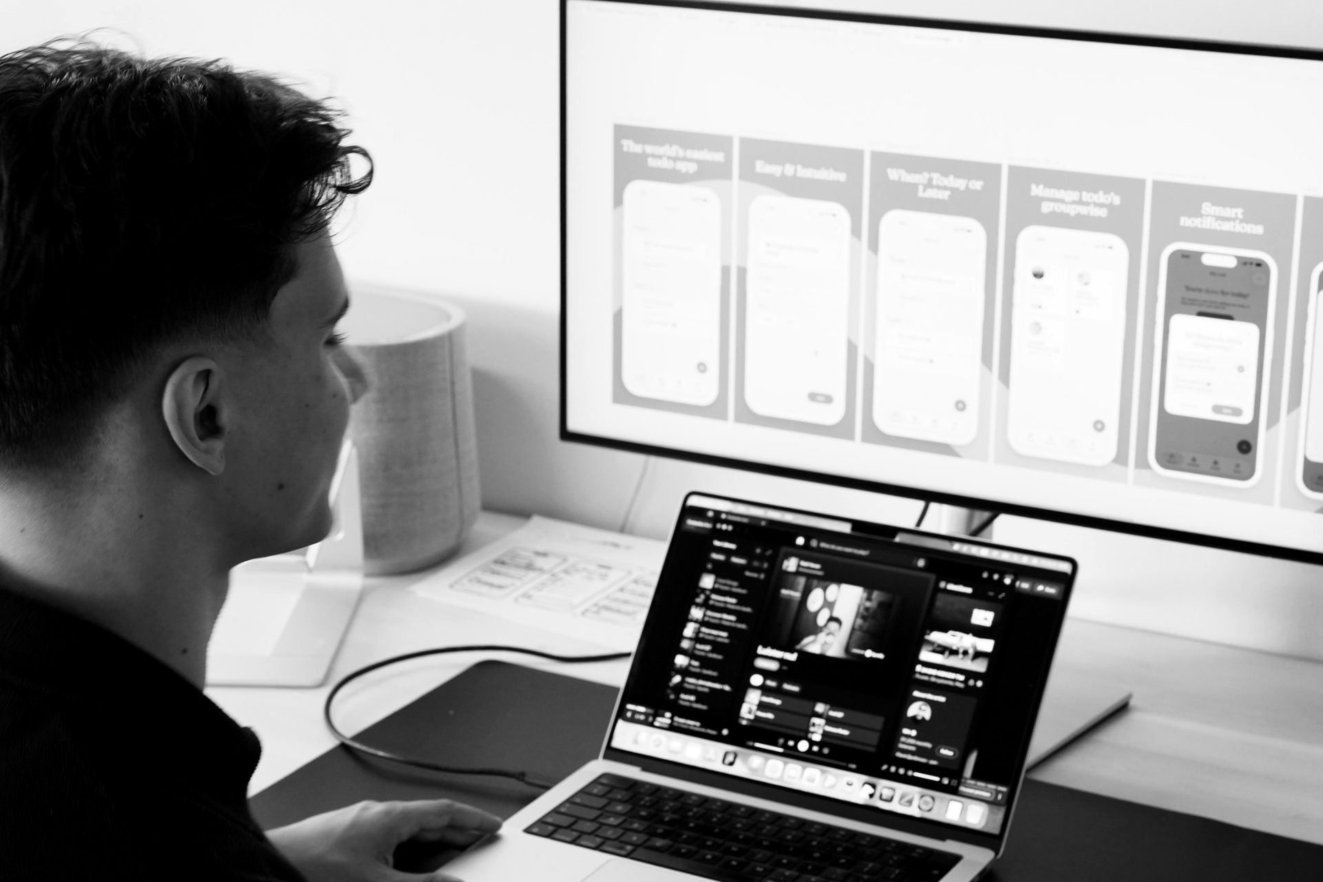 Ontwerper werkt aan app-schermen op een groot scherm boven een laptop